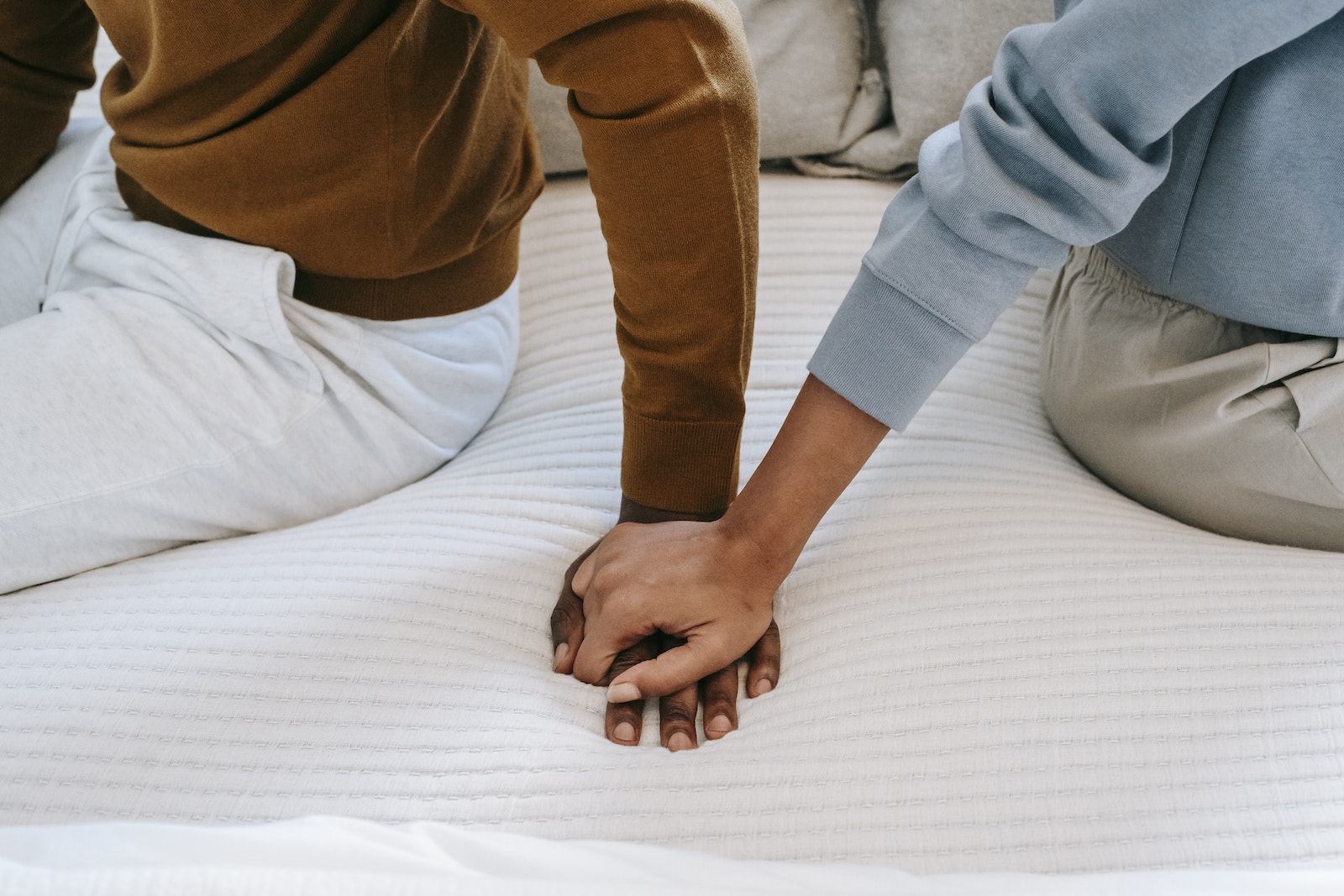 Crop unrecognizable black couple holding hands on bed