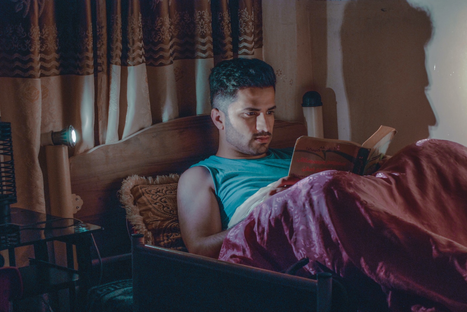 man in blue sleeveless top laying on bed reading book